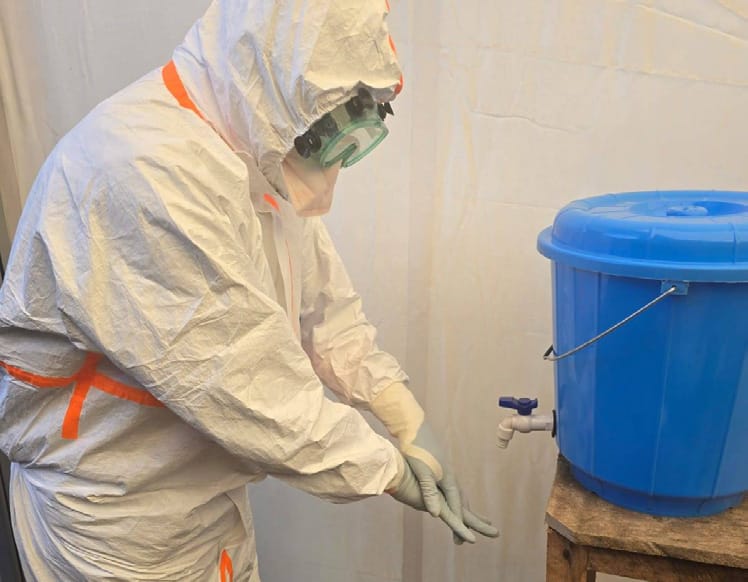 Iqarus clinician in full personal protective equipment at a chlorine handwashing station inside the isolation facility